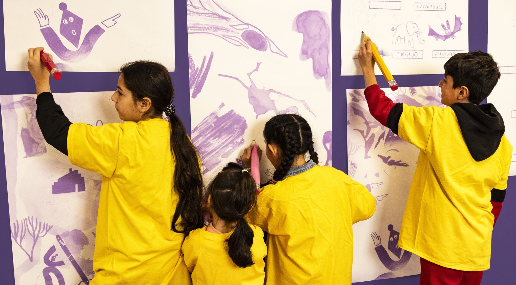 vier kinderen tekenen met grote potloden op de muur